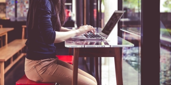 窓際でノートパソコンでブログを書く女性